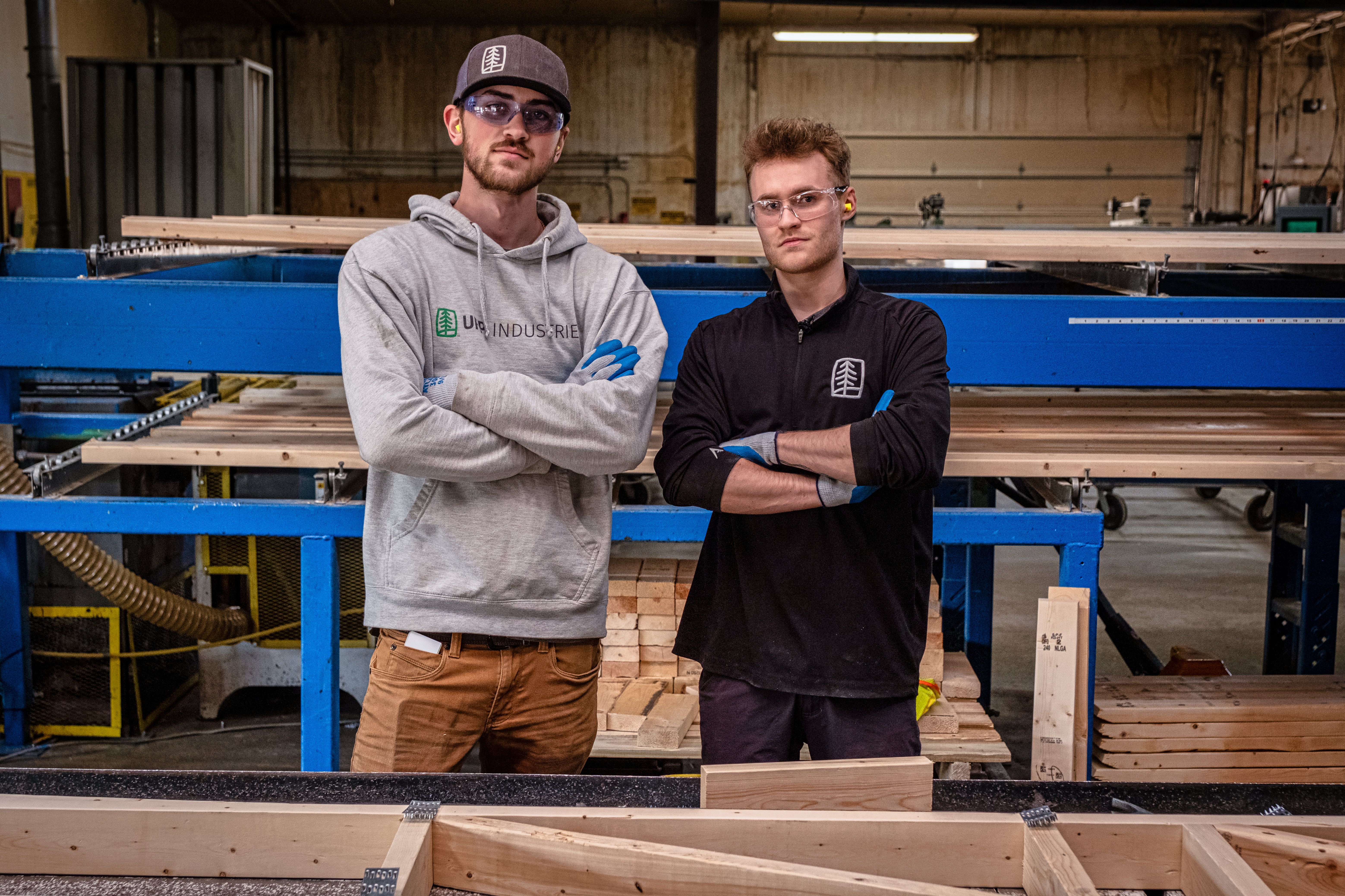 two people standing in a lumber mill with safety glasses and arms crossed