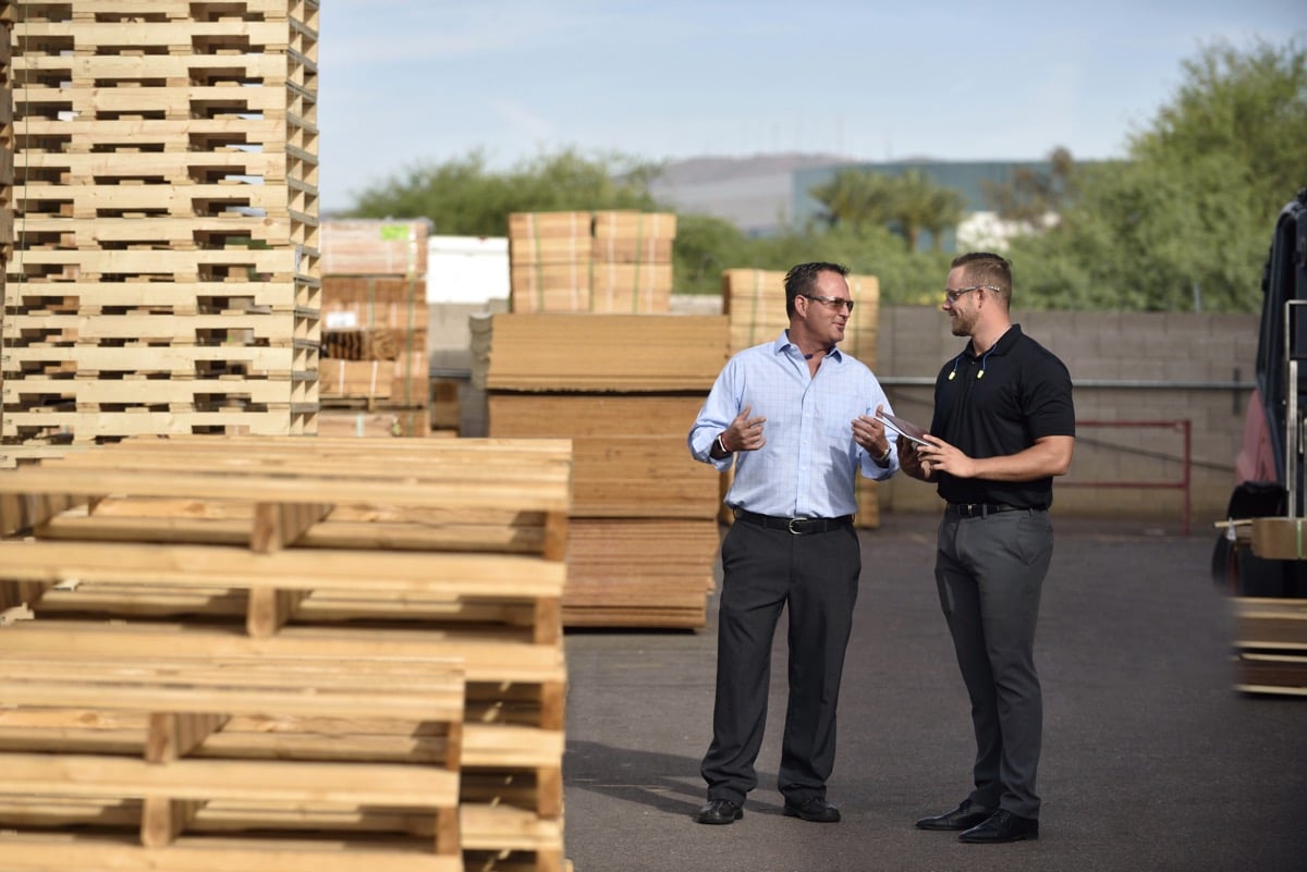 Two people standing outside next to pallets